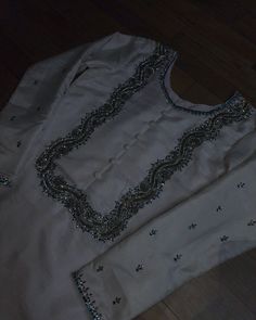 a white shirt with beading on it sitting on top of a wooden floor next to a