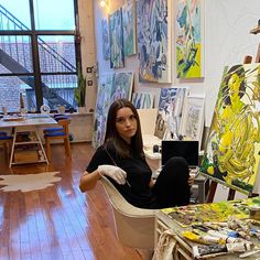 a woman sitting on a chair in front of an easel filled with art work