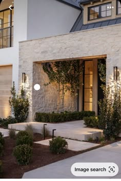 a modern house with stone facade and landscaping in front at night, lit up by outdoor lights