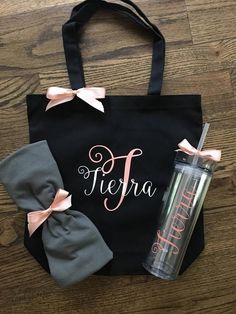 a black tote bag with pink bows and personalized name on it next to a tumbler cup