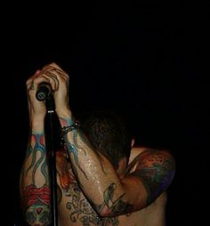 a man with tattoos on his arms and chest holding a microphone in front of him