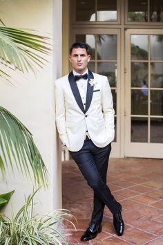 a man in a tuxedo standing next to a wall with plants on it