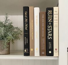 three books are sitting on a shelf next to a potted plant in the corner