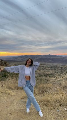 a woman standing on top of a dry grass covered field with her arms spread out