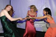 three women in evening dresses dancing together at a formal event with one holding the other's hand