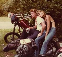 two people are sitting on a motorcycle and one person is standing next to the bike