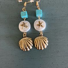 two seashells and starfish earrings are hanging from gold - tone earwires