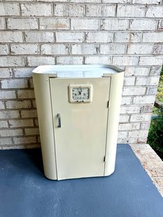 an old white refrigerator sitting in front of a brick wall with a clock on it