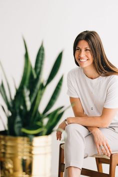 a woman sitting on a chair in front of a potted plant and smiling at the camera