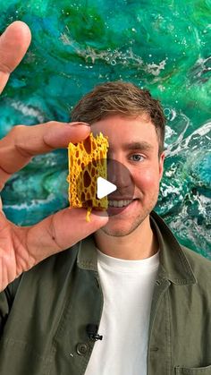 a man holding up a piece of food in front of a green wall with waves