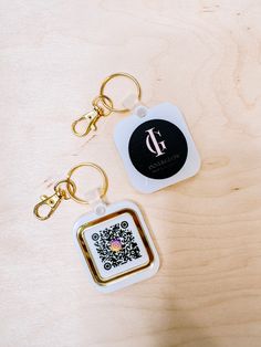 two square key chains sitting on top of a wooden table