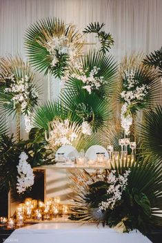 a table topped with lots of white flowers and greenery next to a wall filled with candles