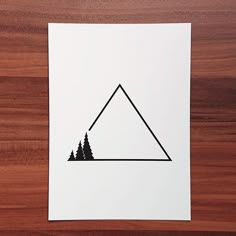 a piece of paper with a triangle and pine trees on it sitting on top of a wooden table