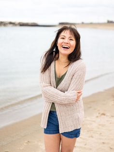 a woman standing on top of a sandy beach next to the ocean with her arms crossed