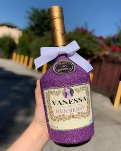 a hand holding up a bottle of hennesy with a purple bow on it