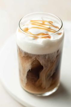 an iced drink with caramel drizzle and whipped cream in a glass on a white plate