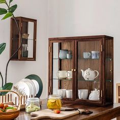 a wooden table topped with dishes and cups next to a glass case filled with drinks