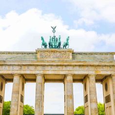 an arch with statues on top in front of trees