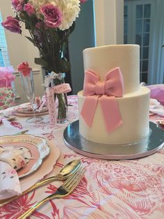 a white cake with pink bows sits on a table next to plates and silverware