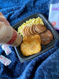 a person is holding a plastic cup over a tray of food on a blue blanket