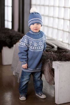 a small child wearing a blue sweater and hat standing in front of a fur rug