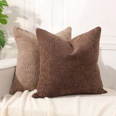 two brown pillows sitting on top of a white couch next to a potted plant