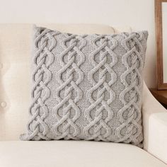 a gray knitted pillow sitting on top of a white couch next to a wooden frame