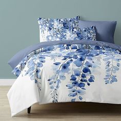 a bed with blue and white flowers on the comforter, pillows and pillow cases