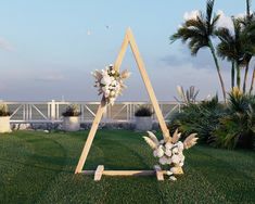 a wooden triangle with flowers on the grass in front of some palm trees and water