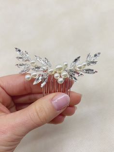 a hand holding a hair comb with pearls and leaves on it's back end