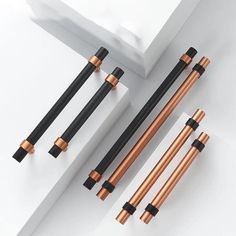 four different types of black and copper handles on a white surface, with one in the middle