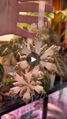 a hand holding a pink and gold snowflake ornament in front of a display case