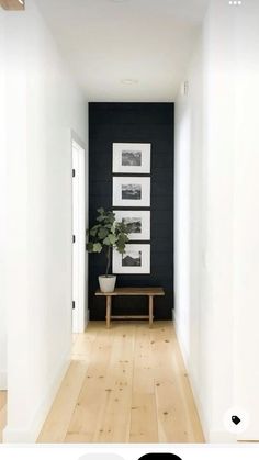 an empty hallway with black walls and white framed pictures on the wall, along with a wooden bench