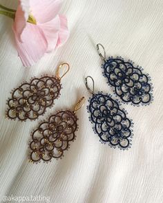 two pairs of earrings sitting on top of a white cloth next to a pink flower