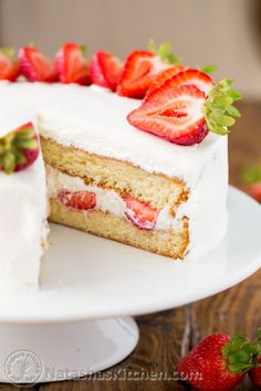 a cake with white frosting and strawberries on top is cut in half to show the inside