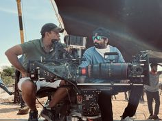 two men sitting in front of a camera on top of a tripod next to another man