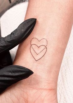 a small heart tattoo on the wrist with dots in it's center and an arrow at the bottom