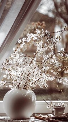 a white vase sitting on top of a window sill next to a cup filled with flowers