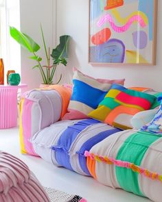 a living room with colorful pillows on the couch and paintings above it, along with other decor items