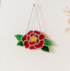 a red and yellow flower hanging from a chain on a white wall next to flowers