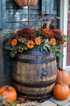 a barrel with flowers and pumpkins sitting on the front porch next to an umbrella