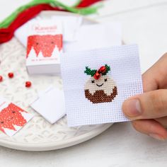 a hand holding a piece of cross - stitch fabric with a christmas decoration on it