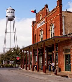 people are standing on the sidewalk in front of an old brick building and water tower