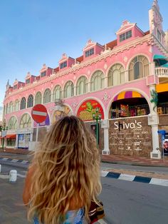 a woman walking down the street in front of a pink building