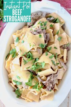 a white bowl filled with pasta covered in meat and parsley on top of a table