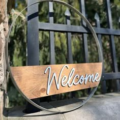 a welcome sign hanging on the side of a black gate with trees in the background