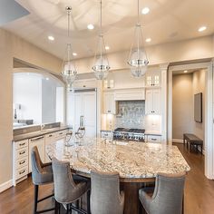 a large kitchen with marble counter tops and white cabinets, along with bar stools