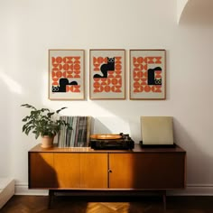 three framed art pieces on the wall above a record player and an old typewriter