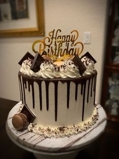 a birthday cake with white frosting and chocolate drizzled on top is sitting on a table