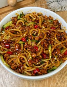 a white bowl filled with noodles and meat on top of a wooden table next to chopsticks